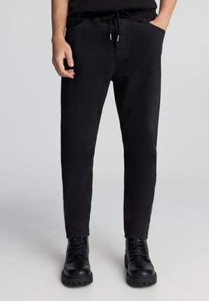Pantaloni jogger in misto cotone neri con vita elastica, cordino e tasche laterali, design a gamba affusolata e leggera trama.