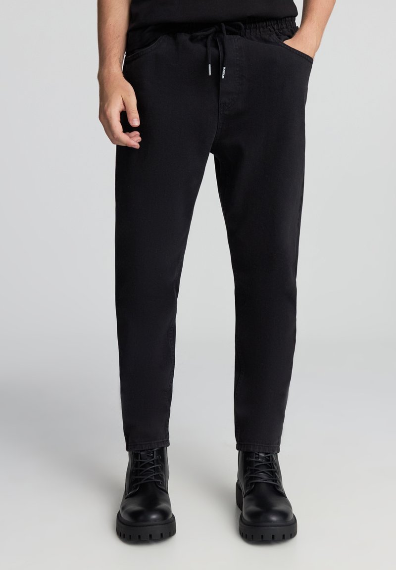 Czarne dresowe spodnie z mieszanki bawełny, z elastycznym pasem, sznurkiem i bocznymi kieszeniami, zwężanym krojem nogawki oraz subtelną teksturą.