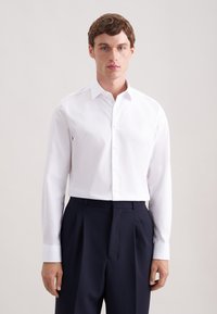 Witte katoenen overhemd met lange mouwen en knopen. Voorzien van een klassieke kraag, recht model en een subtiele glans. Gecombineerd met marineblauwe broek.