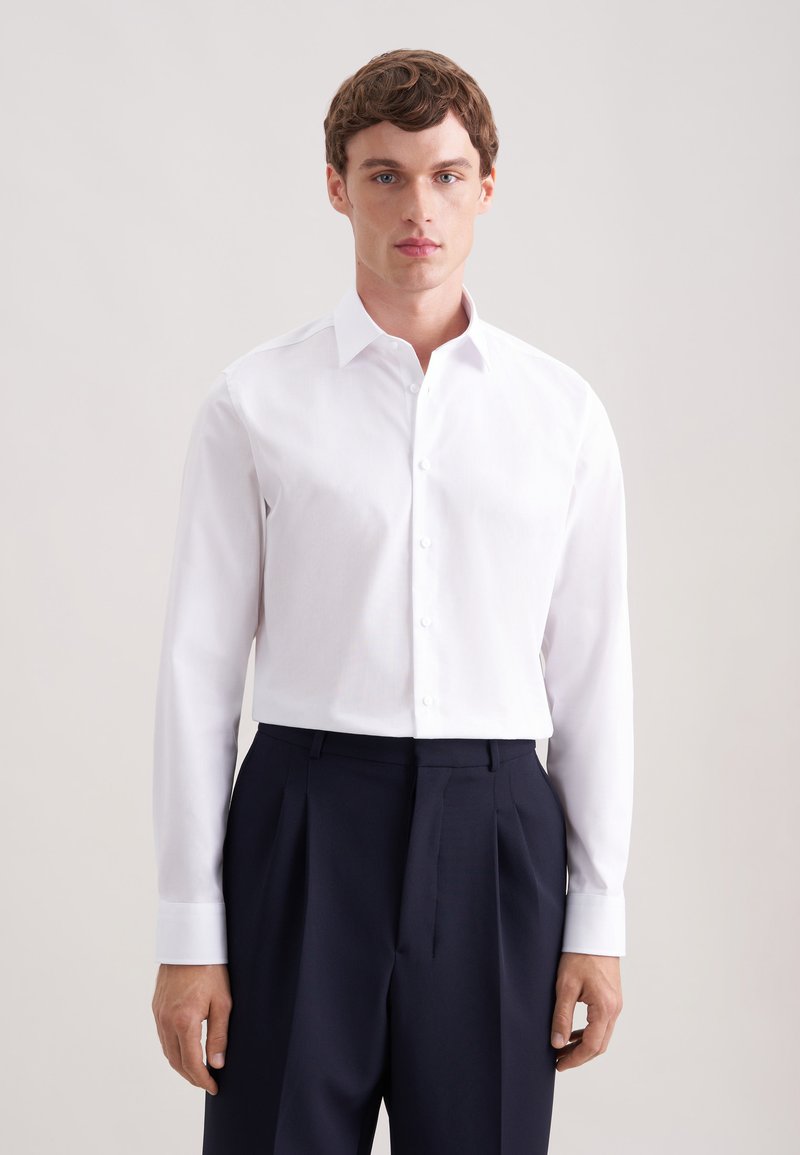 Witte katoenen overhemd met lange mouwen en knopen. Voorzien van een klassieke kraag, recht model en een subtiele glans. Gecombineerd met marineblauwe broek.