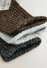 Tre vikta stickade sockor i brunt, grått och svart. Texturerade med ett prickigt mönster och ribbade muddar, som visar olika nyanser och tjocklekar.