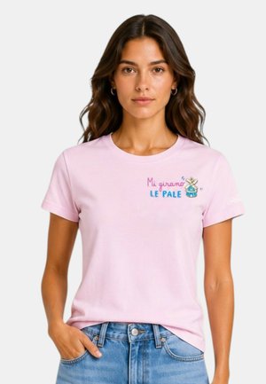 Donna con capelli lunghi e mossi indossa una maglietta rosa chiaro con testo italiano e topo dei cartoni animati, abbinata a jeans blu, mani in tasca.