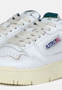 Sneaker bianche in pelle con accenti crema, dotate di una suola in gomma testurizzata, punta perforata, lacci beige e un'etichetta con logo ricamata.