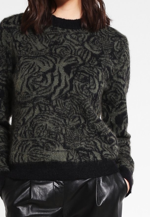 Czarny i zielony sweter w wzory z fakturowaną powierzchnią. Posiada okrągły dekolt oraz ściągacze przy mankietach i dolnym brzegu. Połączony z czarnymi skórzanymi spodniami.