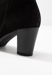 Stivale alla caviglia in suede nero con un tacco cilindrico testurizzato di colore nero. Il tacco ha una leggera inclinazione e presenta sottili scanalature orizzontali.