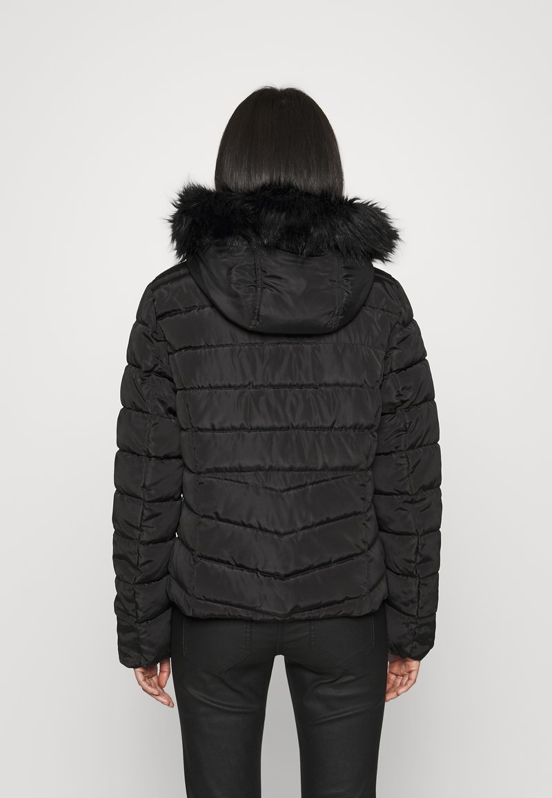 Giacca nera imbottita con cappuccio in pelliccia sintetica, caratterizzata da cuciture orizzontali e polsini elastici, vista da dietro su uno sfondo neutro.