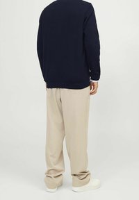 Marinblå texturerad tröja kombinerad med beiga vida byxor och vita skor, med en avslappnad passform och rund halsringning.