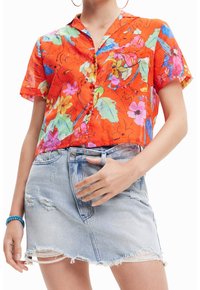 Chemise à manches courtes, orange à fleurs avec des motifs colorés, associée à une jupe en denim léger bleu délavé avec un ourlet effiloché et une fermeture à boutons.