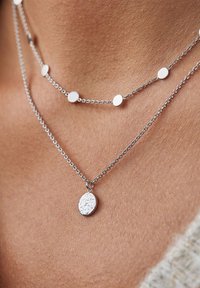 Zilveren gelaagde kettingen met een glanzende ronde schakel met platte schijven en een centrale, getextureerde ovale hanger.