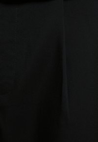 Tejido negro con una superficie suave y ligeramente texturizada. Presenta costuras sutiles y un diseño minimalista, creando una apariencia sólida.