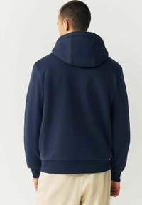 Námornícky modrá mikina s kapucňou z bavlneného zmesi, s veľkou kapucňou, rebrovanými manžetami a spodným lemom, jemnou textúrou a bez viditeľných vzorov alebo loga.