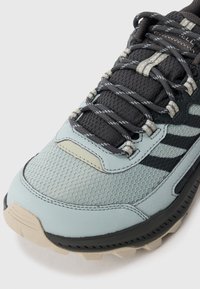 Buty sportowe z teksturowanym jasnoniebieskim wierzchem, czarnymi akcentami, siateczkowymi panelami oraz solidną beżową podeszwą. Widoczne szare sznurówki i przeszycia.