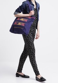 Lila toteväska med geometrisk mönsterbroderi i rosa och orange. Strukturerad design med tjocka remmar och en mjuk textur.