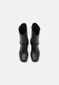Botines de cuero negro con punta cuadrada plana, que presentan acentos de tachuelas en el caño y un detalle de hebilla en el lateral.