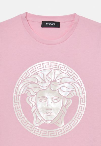 Camiseta de algodón rosa con un gran gráfico de Medusa en plata metálica centrado dentro de un borde circular con diseño de llaves griegas. Escote redondo, mangas cortas.