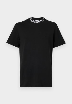 Schwarzes Kurzarm-T-Shirt mit weißem "LACOSTE" Text am Kragen und einem dezenten schwarzen Lacoste-Logo auf der linken Brust.