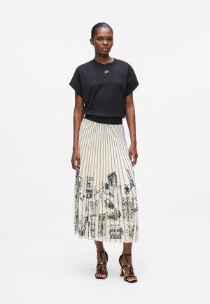 Zwart kortemouwen top in combinatie met een geplisseerde beige rok met zwarte architecturale lijntekeningen. Zwarte haksandalen maken de outfit compleet.