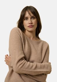 Beige gebreide trui met een relaxte pasvorm, ronde halslijn en lange mouwen. De stof lijkt zacht met een subtiele textuur.