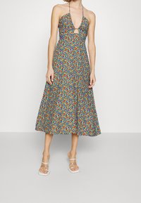 Květinové midi šaty s halter výstřihem, modrým podkladem, barevným květinovým vzorem a detailem s otvorem, vyrobené z lehkého materiálu. Průhledné sandály.