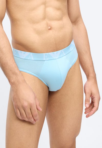 Ανδρικός κορμός με ανοιχτό μπλε εσώρουχο με ελαστική μέση με λογότυπο, σε απλό ανοιχτό φόντο.