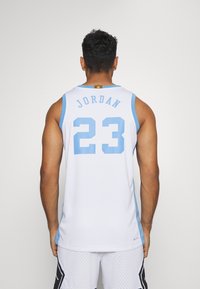 Maillot de basketball blanc pour homme avec des accents bleu clair. Porte les inscriptions "JORDAN" et "23" imprimées en bleu au dos. Fabriqué en matériau respirant.