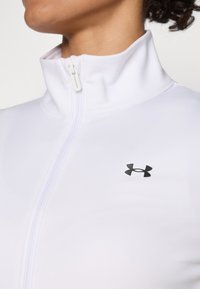 White zip-up jacket made of smooth, stretchy fabric. Features a high collar and a black logo on the left chest area.