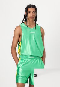 Žalias be rankovių sportinis marškinėlis ir šortai iš blizgaus audinio, su juodais ir geltonais juosteliais bei Adidas logotipu.