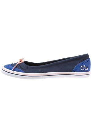 Marineblaue Ballerina aus Canvas mit hellblauen Wildleder-Akzenten, rosa Schleife an der Spitze, weißer Gummisohle und kleinem besticktem Krokodil-Logo nahe der Ferse.
