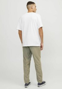 Weißes Baumwoll-T-Shirt mit kurzen Ärmeln, kombiniert mit hellen Khaki-Hosen und navyfarbenen Sneakers. Das Outfit hat eine lockere Passform und ein einfaches Design.