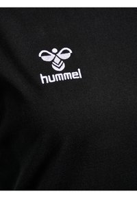 Tricou negru cu un logo brodat alb în formă de colibri și textul "hummel", realizat dintr-un material moale cu o textură netedă.