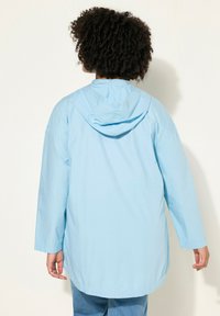 Chaqueta ligera de color azul claro con capucha, mangas largas y un corte relajado. La tela parece suave y ligeramente brillante.