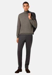 Pilkas turtleneck megztinis derinamas su tamsiomis, pritaikytomis kelnėmis. Megztinis turi lygų paviršių, o kelnės puošia subtilus languotas raštas. Rudos zomšinės bateliai.