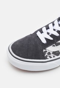 Musta mokkasneakerit, joissa on valkoiset nauhat ja kumipohja. Sivussa on harmaata kuviollista kangasta ja mustaa reunanaita.