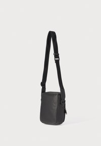 Černá crossbody taška vyrobená z hladké tkaniny, s nastavitelným popruhem a kapsou na zip na boku. Kompaktní čtvercový tvar.