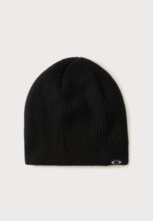 Bonnet en tricot noir avec une petite étiquette de logo noire et blanche sur le bord inférieur, sur un fond clair uni.