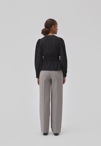 Black textured blouse with puff sleeves and a cinched waist, paired with light gray wide-leg trousers and black shoes, shown from behind.