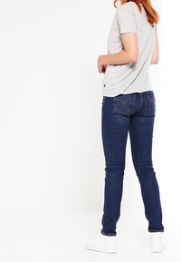Slim-fit mörkblå denimjeans med midja i medelhöjd, parat med en ljusgrå t-shirt med kort ärm och vita sneakers.