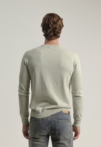 Suéter gris claro de manga larga y cuello redondo, mostrado desde la parte de atrás. Usado con jeans azules con bolsillos traseros.