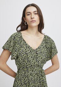 Floral dress with short flutter sleeves, featuring a V-neckline. Black fabric adorned with small green and white floral patterns.