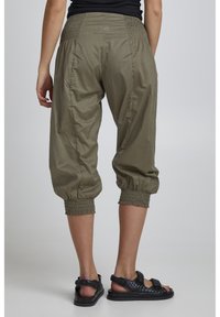 Pantaloni corti verde oliva con orlo ed elastico in vita, caratterizzati da una texture liscia e dettaglio arricciato, abbinati a sandali neri.