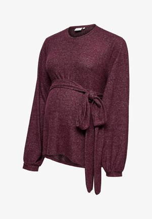 Vīna sarkana grūtnieču blūze ar garām piedurknēm, apaļu kaklu un piesietu vidukļa detaļu. Izgatavota no mīksta, teksturēta auduma, nodrošinot komfortu.