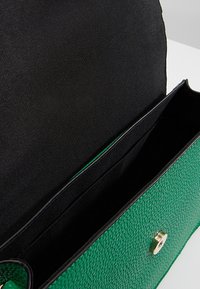 Grön texturerad handväska med svart inredning, som har en magnetisk tryckknapp och ett stort fack, designad för mångsidig användning.