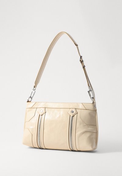 Sac à main en cuir beige avec un design structuré, deux compartiments zippés et une bandoulière amovible. Présente des accents en métal argenté.
