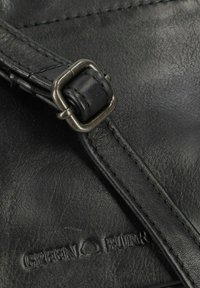 Dettaglio di una borsa in pelle nera caratterizzata da una superficie testurizzata, una tracolla regolabile con fibbia in metallo e il logo impresso "GREEN BURR".