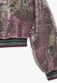 Růžový a stříbrný rukáv pokrytý flitry s multibarevnou glitrovou manžetou se žebrovaným vzorem ve zelených, modrých, fialových a červených pruzích.