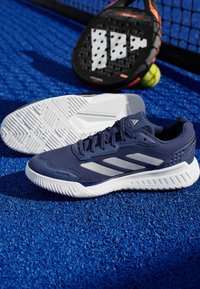 Granatowe buty sportowe z siateczkową cholewką, z srebrnymi paskami, teksturowaną białą podeszwą i brandingiem "Cloudfoam". Na tle niebieskiego boiska.