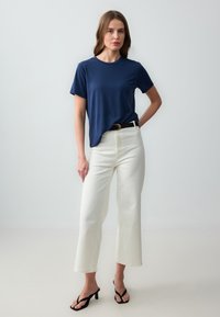 Marineblauwe T-shirt met korte mouwen, ontspannen pasvorm, gecombineerd met hoge witte wijde broek en zwarte hoge flip-flops. Minimalistisch ontwerp.