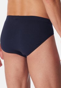 Dunkelblaue Baumwollslips mit einer glatten Textur, niedrigem Schnitt, elastischem Bund und sichtbaren genähten Saumdetails an den Seiten.
