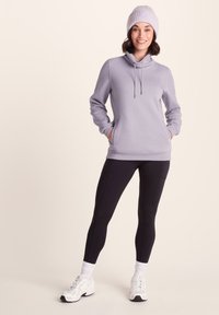 Light purple hoodie with drawstrings, kangaroo pocket, paired with black leggings. Model wearing white sneakers and a ribbed light purple beanie.