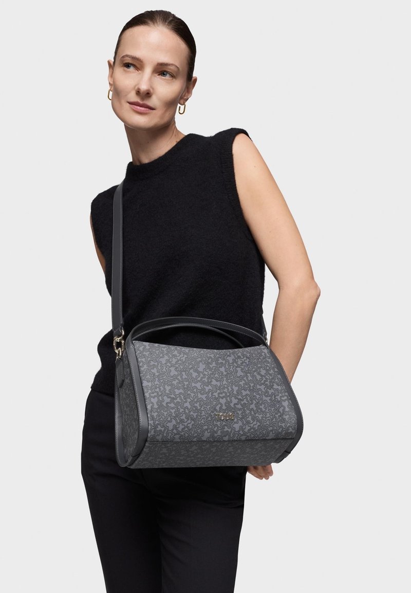 Szara torebka o strukturalnym projekcie, z tłoczonym wzorem i gładkimi skórzanymi akcentami. Regulowany pasek i złote logo z przodu.